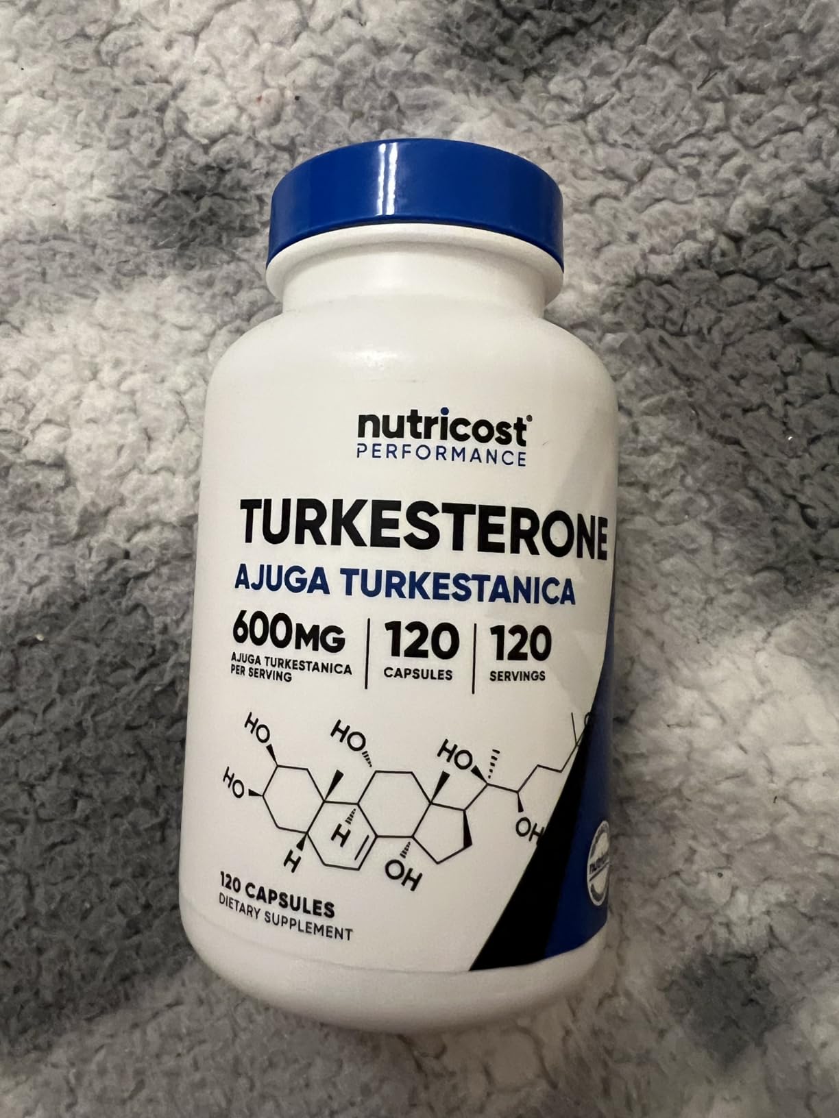 Nutricost Turkesterone bottle, Ajuga turkestanica 600 mg, 120 capsules, lying on a gray fleece blanket