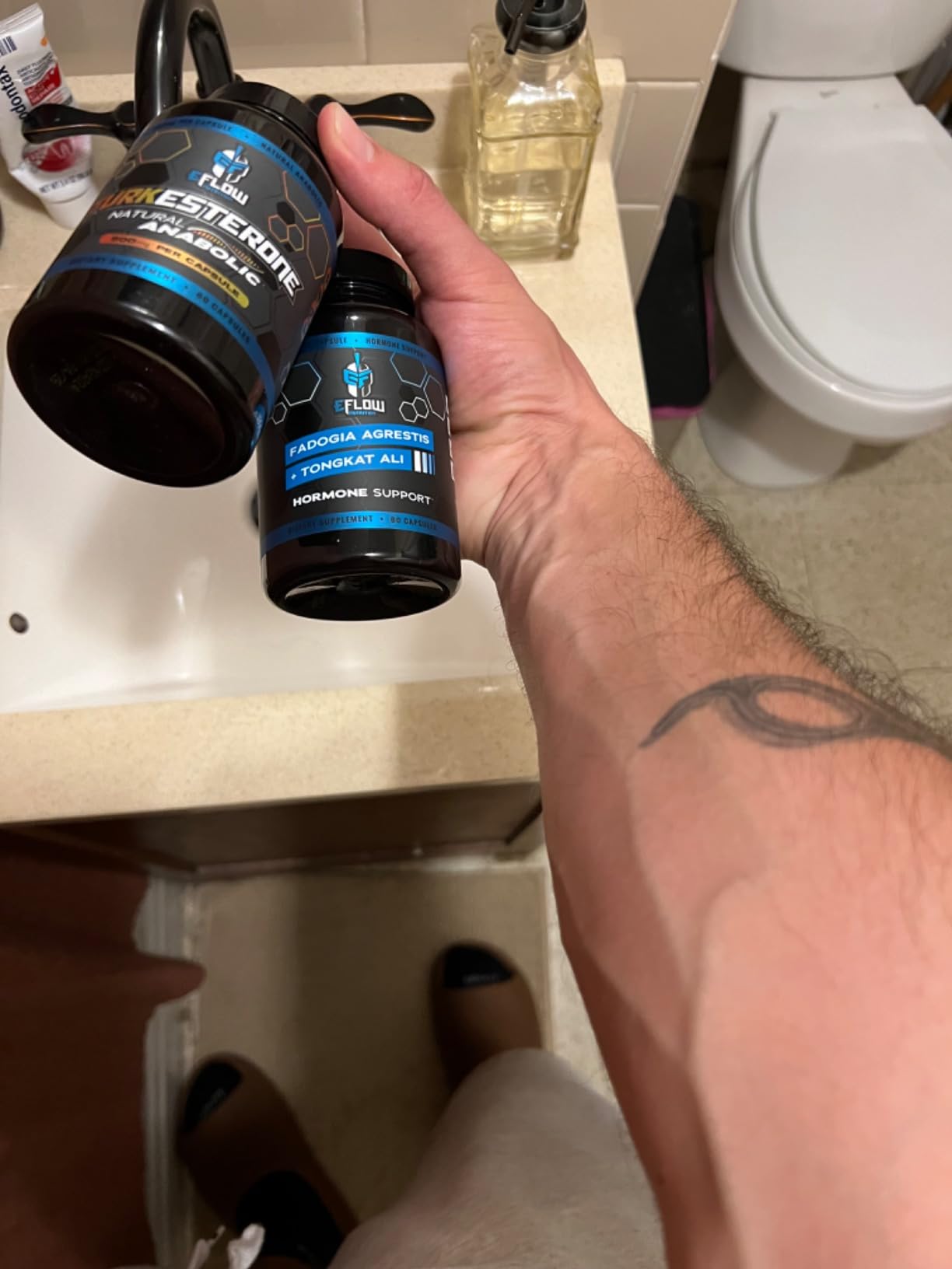 Customer holding eFlow Turkesterone and Fadogia Agrestis with Tongkat Ali bottles over a bathroom sink